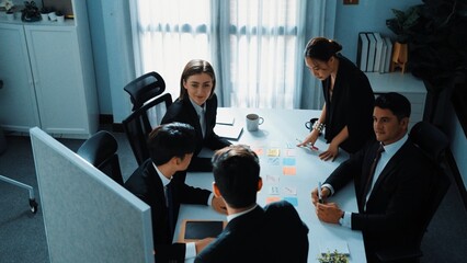 Fototapeta premium Top view of smart businessman putting sticky note on whiteboard while marketing team brainstorm creative idea at meeting room. Leader explain startup project to group of diverse investor. Directorate.