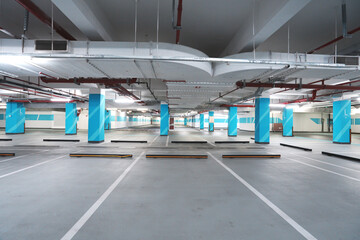 Naklejka premium Empty underground parking lot with blue columns and marked parking spaces