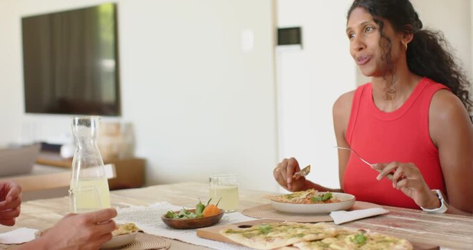 African American woman in red sleeveless top talking, cutting flatbread at dining table with carafe