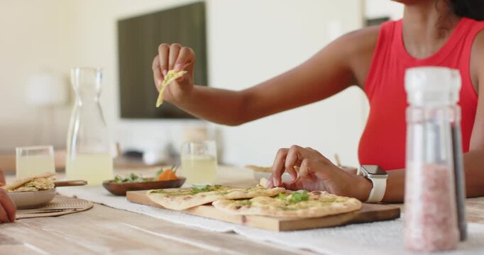 Couple sharing flatbread at dining table to share meal, woman in red top offering, man eating