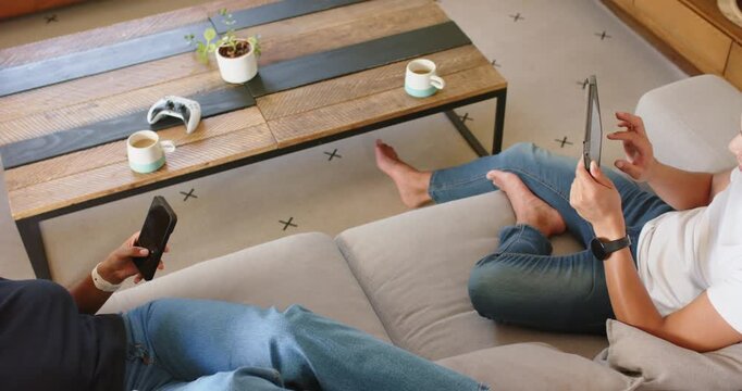 African American couple at home, woman arriving, man tapping tablet, she scrolling phone relaxing