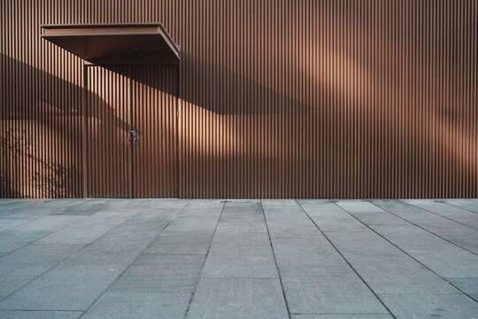 Brown vertical corrugated metal wall with doorway overhang and dramatic shadow patterns