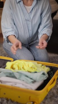 Careful hands of woman neatly fold and pack clothes into bright yellow suitcase, diligently prepare for an upcoming journey, vacation, or business trip at home.Travel preparation, trip organization