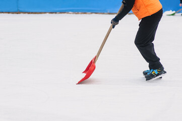 Obraz premium A young man, a teenager, clears snow with a shovel in winter at an ice rink for sports.