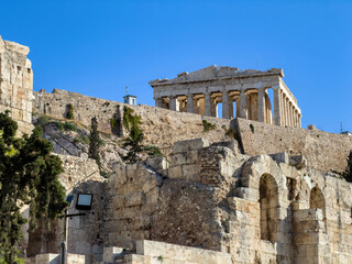 Fototapeta premium Parthenon above Herodeion arches on Acropolis hill in Athens, Greece. Ancient stone walls and arcades, blue sky