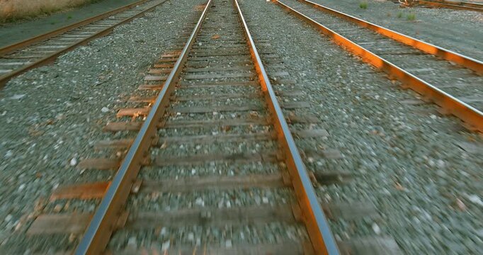 Train tracks run parallel in an urban setting ground is covered with stones, small plants grow between rails.