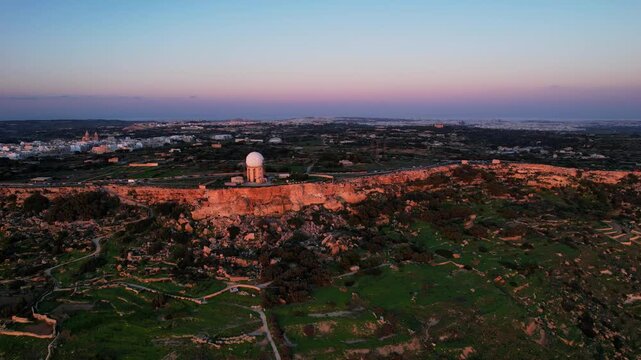 Aerial drone view of the Highest point of Malta at Dingli Cliffs, beautiful lush green grass and rock formations with a steep drop to the sea at sunset, golden hour. Sun giving the golden glow