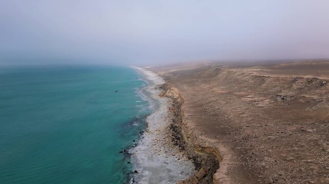 Aerial drone footage of a long sandy coastline in Aktau, Mangystau, Kazakhstan, bordered by low cliffs on one side and the Caspian Sea on the other. Empty rocky beach and vast open space create 