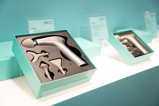 WARSAW, POLAND - FEBRUARY 18, 2026: An editorial close-up of SKG brand percussion massage guns, specifically the X7-E model, displayed in retail packaging at a trade show