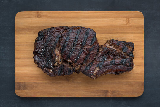 A large, well-charred smoked beef steak on a wooden plank after being barbecued before serving.