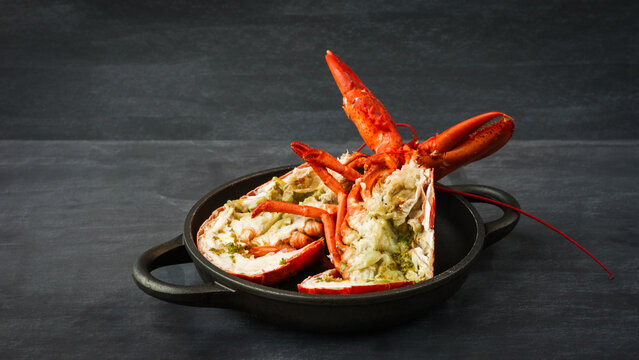 Two halves of grilled red lobster in a black bowl with a dark background