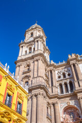 Fototapeta premium Low angle view of Malaga Cathedral bell tower and colorful historic building facade