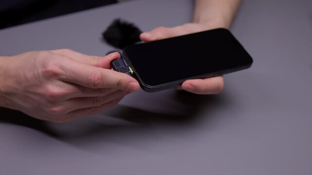 Content creator hands setting up professional audio recording system by plugging wireless lavalier microphone receiver with adapter into mobile phone for interviews, close-up, slow motion.