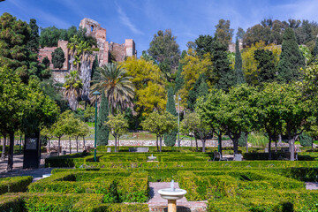 Malaga Spain symmetrical garden design with manicured hedges and stone fountains in the Pedro Luis Alonso Gardens under the historic Alcazaba of Malaga fortification.