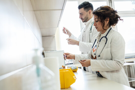 Two doctors prepare vaccines in a treatment lab, working carefully with medical equipment. The scene feels sterile and focused, highlighting precision and teamwork.