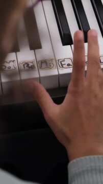 Close up view of a young child's hand learning to play the piano. Kid's fingers pressing the white keys with solfege notes written on them