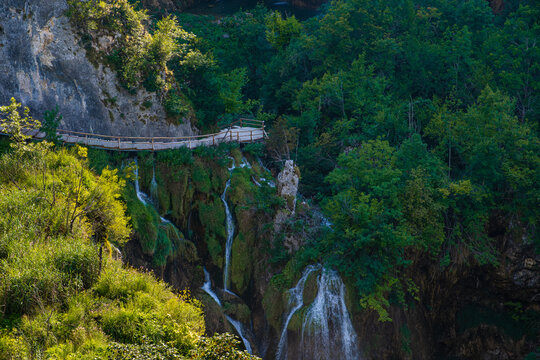 A waterfall landscape with a wooden walkway above it on a sunny summer day