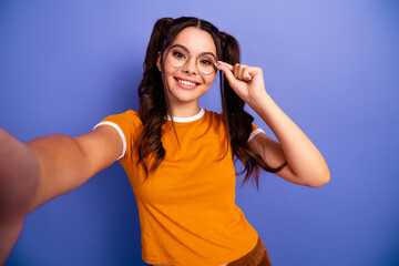 Fototapeta premium Young female student smiling taking a selfie wearing glasses against blue background in orange shirt for fashion lifestyle and advertising