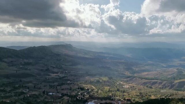 Scenic view of rolling hills and valleys under a dramatic sky with clouds in the Province of Enna, showcasing the natural beauty of the Sicilian landscape