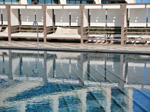 Luxury hotel pool deck with modern cabanas and reflections in the water. Upscale
resort rooftop terrace with daybeds and geometric tiles in Malta. Minimalist boutique
travel photography of Mediterrane