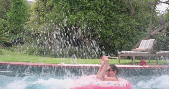 Diverse female friends in bikinis, one jumping off pool edge, splashing, trying to flip donut float