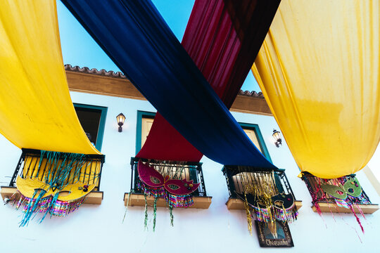 Borogod&oacute; brasileiro no Carnaval de Tiradentes: fachadas hist&oacute;ricas e cores.

 Fachada colonial em Tiradentes decorada com tecidos vibrantes e m&aacute;scaras carnavalescas sob c&eacute;u azul. 