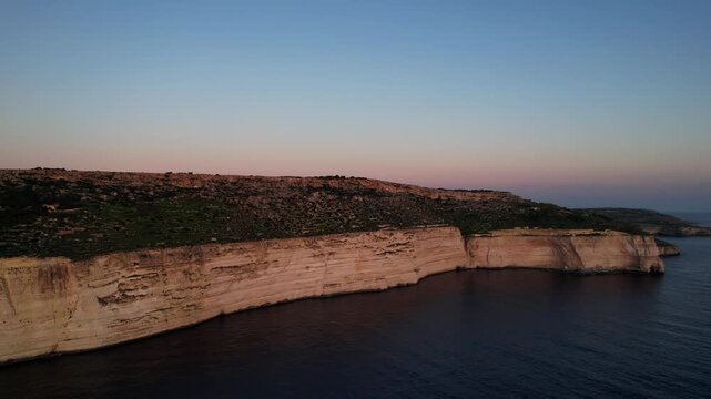 Aerial drone view of the Highest point of Malta at Dingli Cliffs, beautiful lush green grass and rock formations with a steep drop to the sea at sunset, golden hour. Sun giving the golden glow