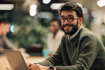 Young man smiling working on laptop in office