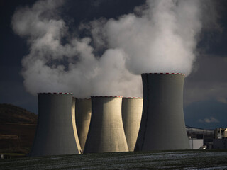 Massive cooling towers of power plant emitting thick steam against dark dramatic storm sky