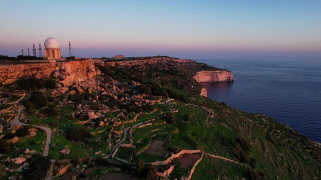 Aerial drone view of the Highest point of Malta at Dingli Cliffs, beautiful lush green grass and rock formations with a steep drop to the sea at sunset, golden hour. Sun giving the golden glow