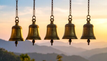 Obraz premium Five antique bells suspended from above, ringing out over serene mountains at sunrise from a high vantage point.