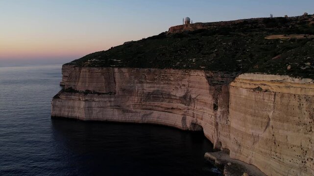 Aerial drone view of the Highest point of Malta at Dingli Cliffs, beautiful lush green grass and rock formations with a steep drop to the sea at sunset, golden hour. Sun giving the golden glow