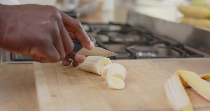 Knife tip touching banana hands are making short downward cuts producing slices for recipe at stove