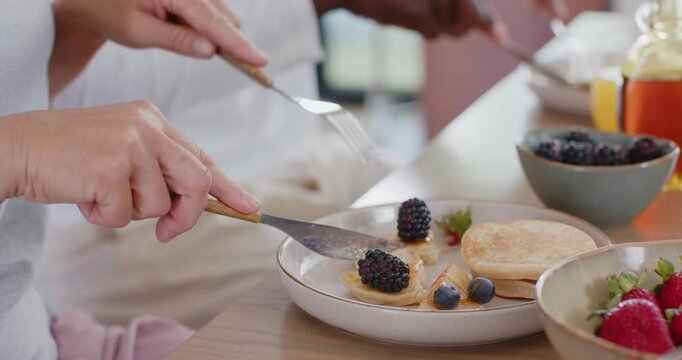 Diverse senior couple pressing fork, cutting pancake using knife, lifting berry bite, sharing meal