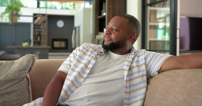Adult African American man sitting on couch, camera pulling in, turning head, smiling, laughing