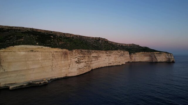 Aerial drone view of the Highest point of Malta at Dingli Cliffs, beautiful lush green grass and rock formations with a steep drop to the sea at sunset, golden hour. Sun giving the golden glow