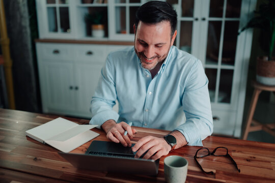 Professional man happily working on laptop at home, smiling, browsing content, remote work and flexibility concept