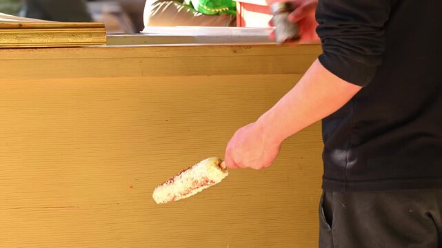 Authetic Mexican street food, hands adding chili power to traditional Elote