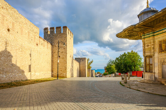 The historic stone walls of the Topkapi Palace near the Imperial Gate entrance, with the Fountain of Sultan Ahmed III in front, in Sultanahmet District of Istanbul.
