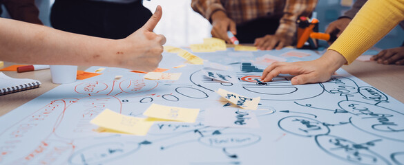 A dynamic workshop scene showcasing multiple hands engaged in writing and planning on a large paper...