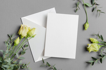 Blank invitation or greeting card mockup with white envelope and yellow roses on gray background, featuring ample copy space for text or design elements