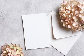 Blank invitation or greeting card mockup with an envelope and dried hydrangea flowers on a textured gray background for design purposes