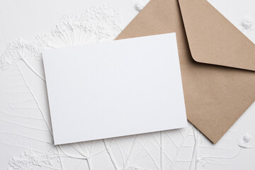 Blank wedding invitation card mockup placed on textured white background with brown envelope, ideal for personalized design and customization for special occasions