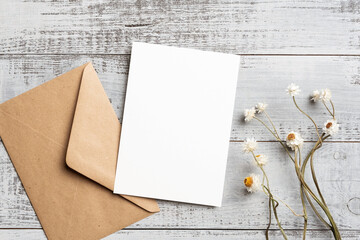 Blank invitation card mockup with envelope, dried flowers decoration on wooden background, card with copy space for design presentation