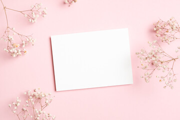 Horizontal white blank card mockup surrounded by delicate baby breath flowers on a soft pink background, perfect for wedding stationery or greetings, flat lay