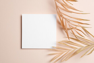 Square white blank card placed on a soft beige background with dried palm leaves, ideal for wedding invitations, natural-themed stationery, or boho card mockups
