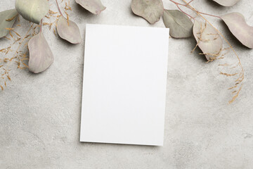 Blank white card mock up with dried eucalyptus leaves on a textured gray background, providing a minimalist design space for creative projects and visual presentations