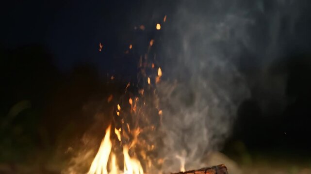 Close-up of a campfire at night with glowing embers and rising smoke