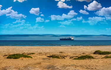 Naklejka premium Cargo ship and coastal fog over the Skeleton Coast, Namibia. Bright blue sky with scattered clouds