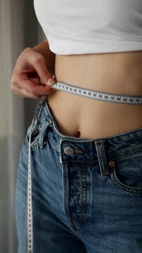 Woman measuring waist with tape, tracking weight loss progress and achieving fitness goals.